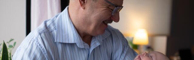 Something happens to a man’s face when he holds his grandchild for the first time that is different from the face he made when he held his own child — and the difference is visible in these 8 ways, and every one of them traces to something he now knows that he didn’t know the first time